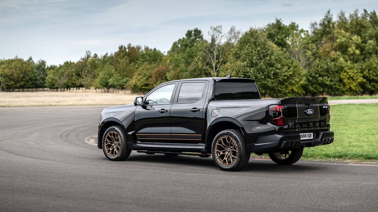 Πλάγια πίσω όψη του Ford Ranger MS-RT Champion Edition σε πίστα, που δείχνει το διπλοκάμπινο αμάξωμα, τα πλευρικά μαρσπιέ και τις χρυσές σφυρήλατες ζά