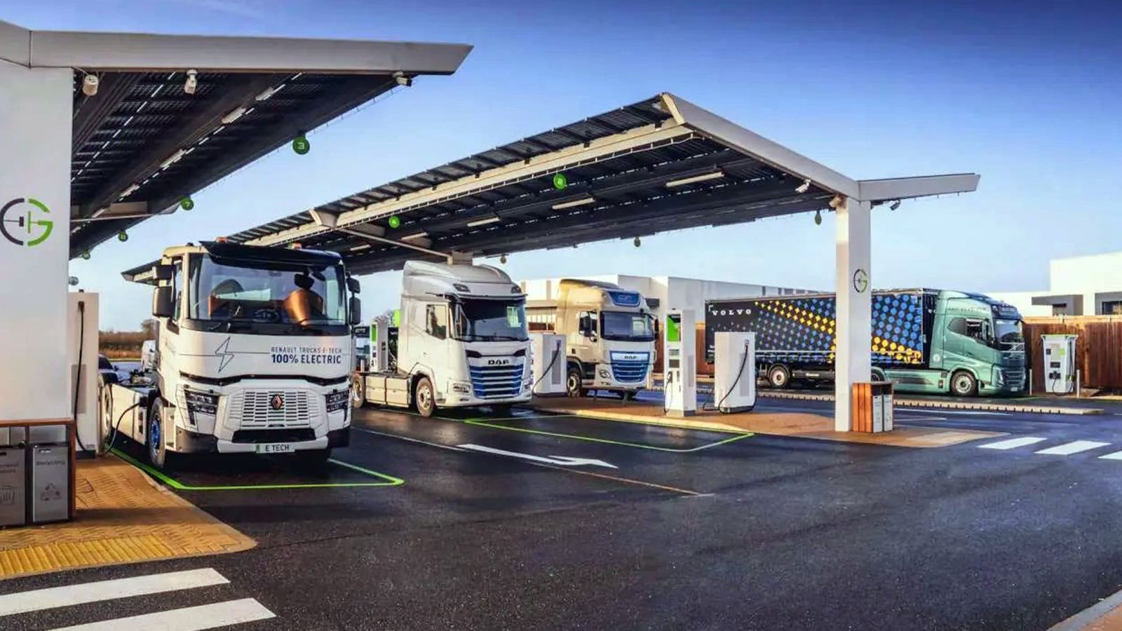 Ηλεκτρικά φορτηγά Renault Trucks, DAF και Volvo σε σταθμό φόρτισης με φωτοβολταϊκά στέγαστρα.