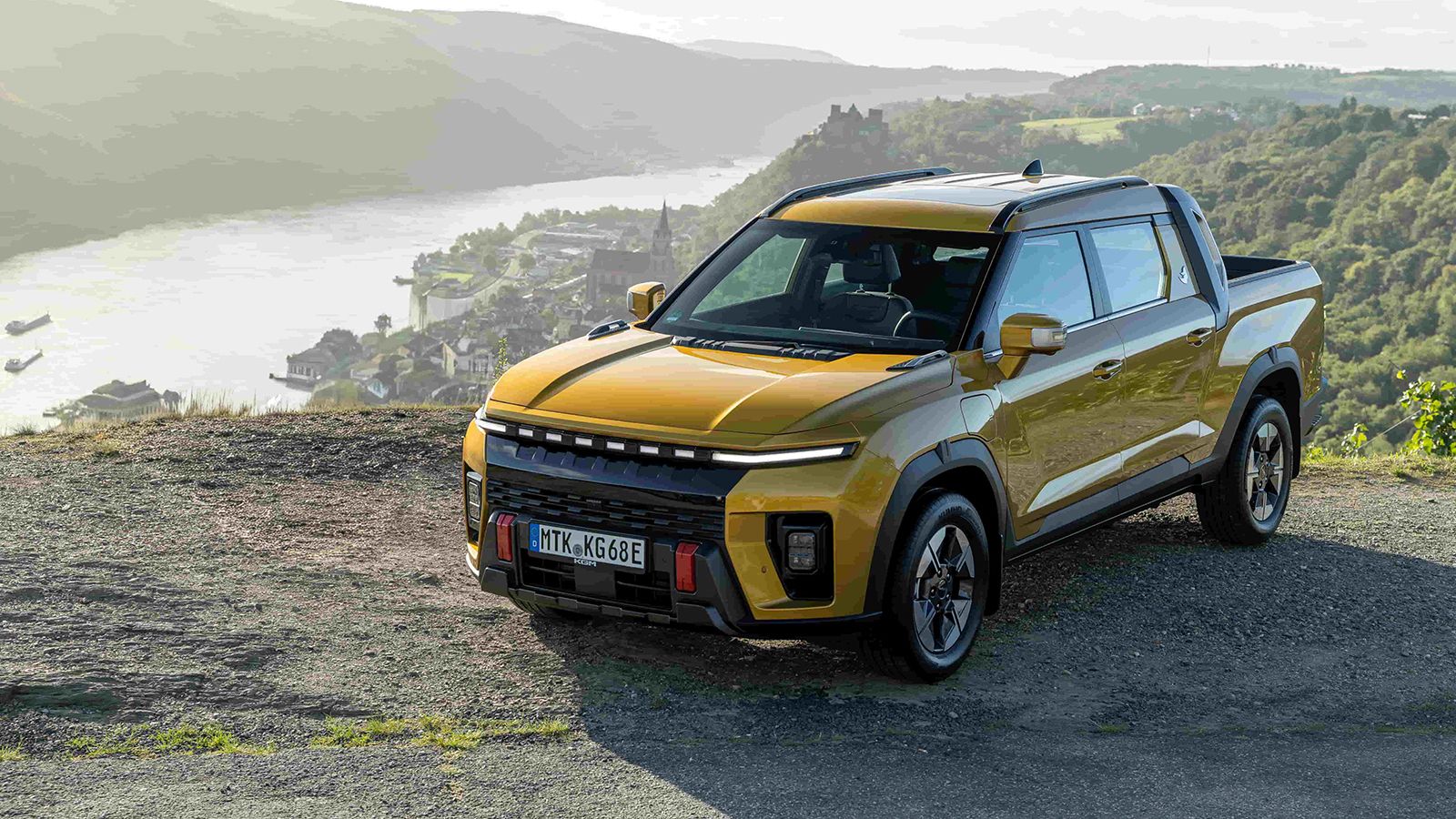 Κίτρινο KGM Musso EV σε εμπρός πλάγια όψη, με φόντο ποτάμι.